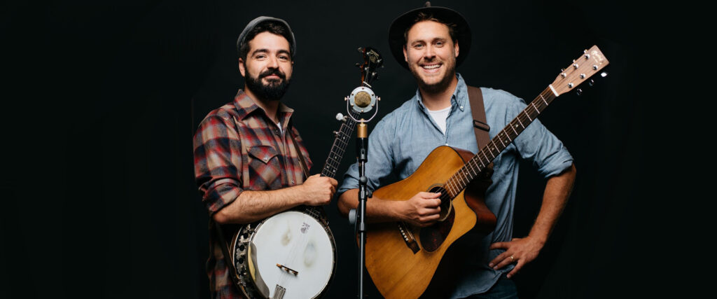 The Okee Dokee Brothers holding Martin acoustic guitar and resonator banjo behind a microphone and against a black background